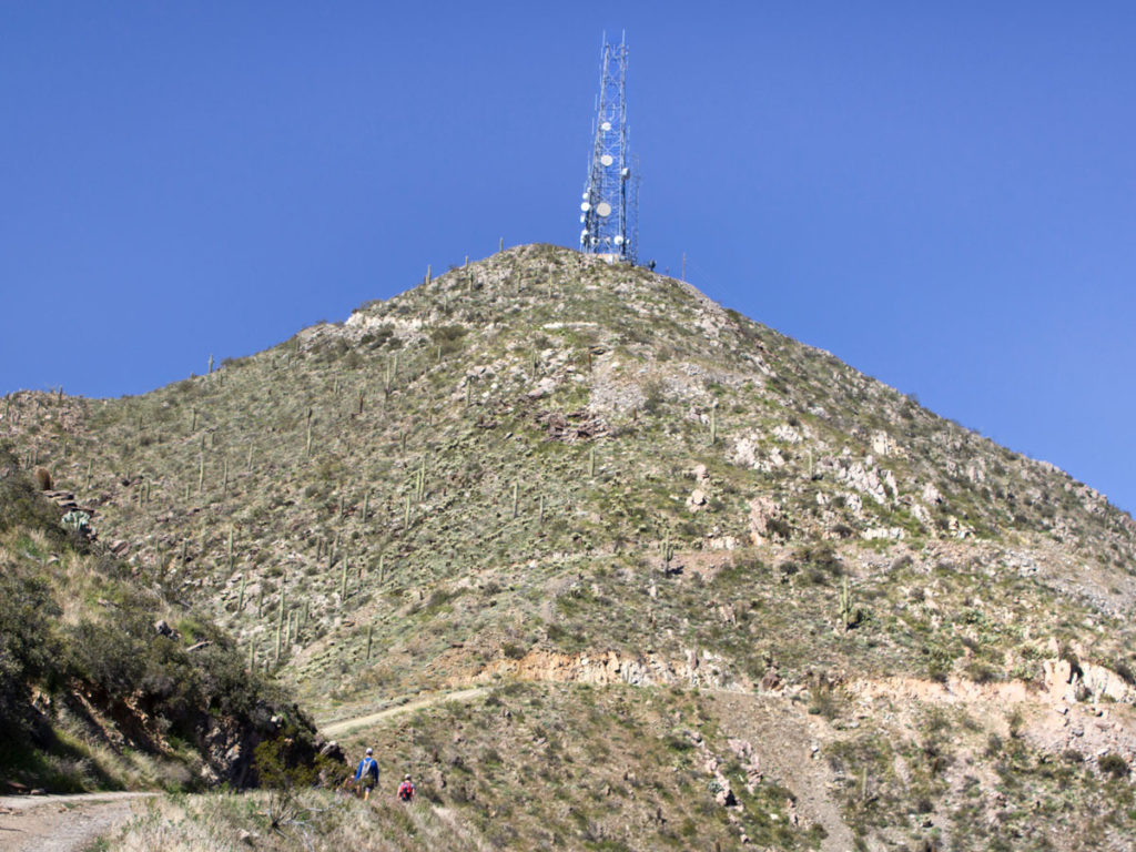 Hikers approaching the top of Thompson Peak; on the Thompson Peak Hiking Trail in the McDowell Mountains; Satellite Towers crown the peak. Phoenix Area Hikes; Difficult Hikes; Fountain Hill; Arizona. Copyright azutopia.com. No use without permission.